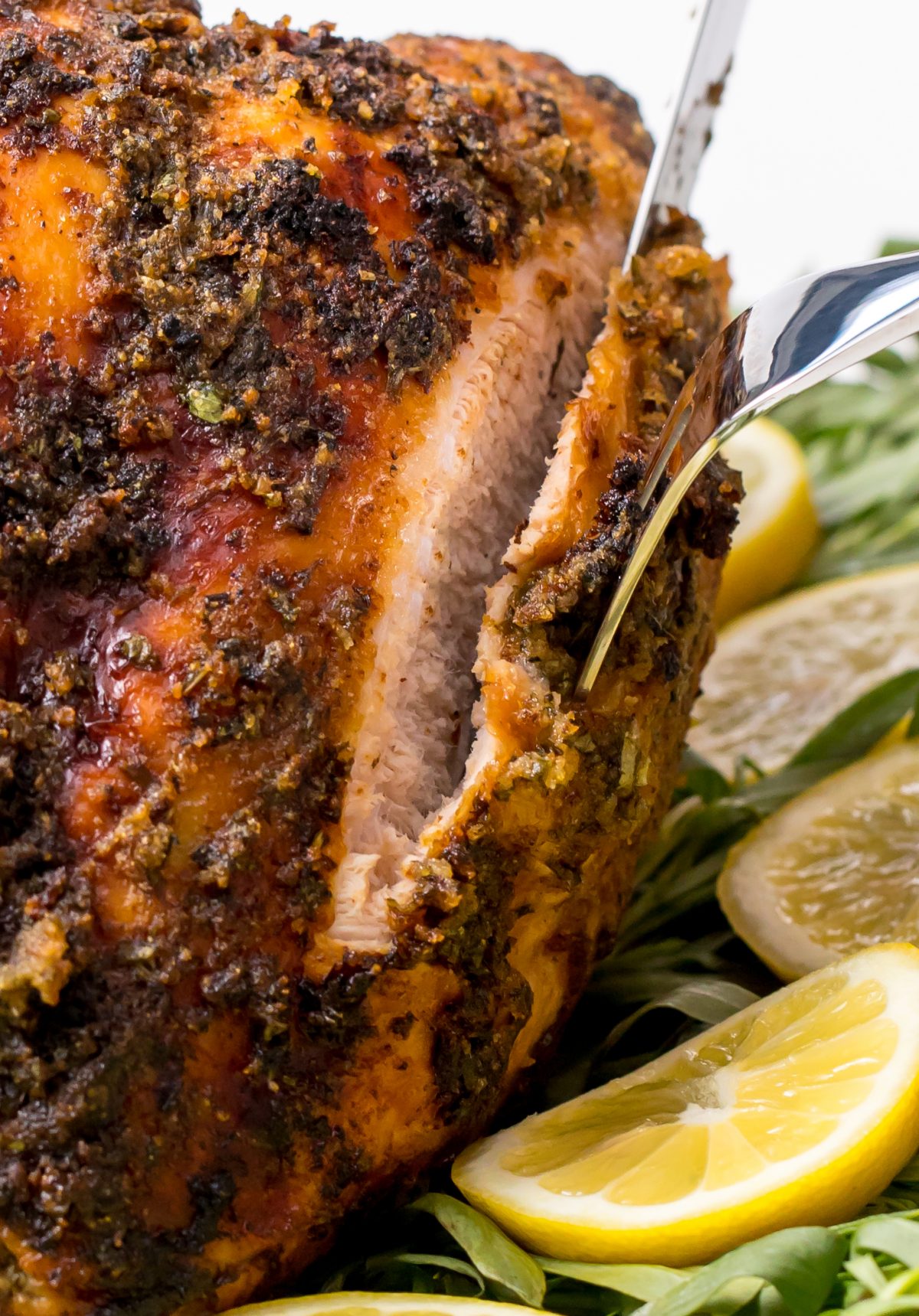 Tender and juicy grilled turkey breast- cutting a plated grilled turkey with sauce on on a bed of grass and lemons on a white table using a knife and fork