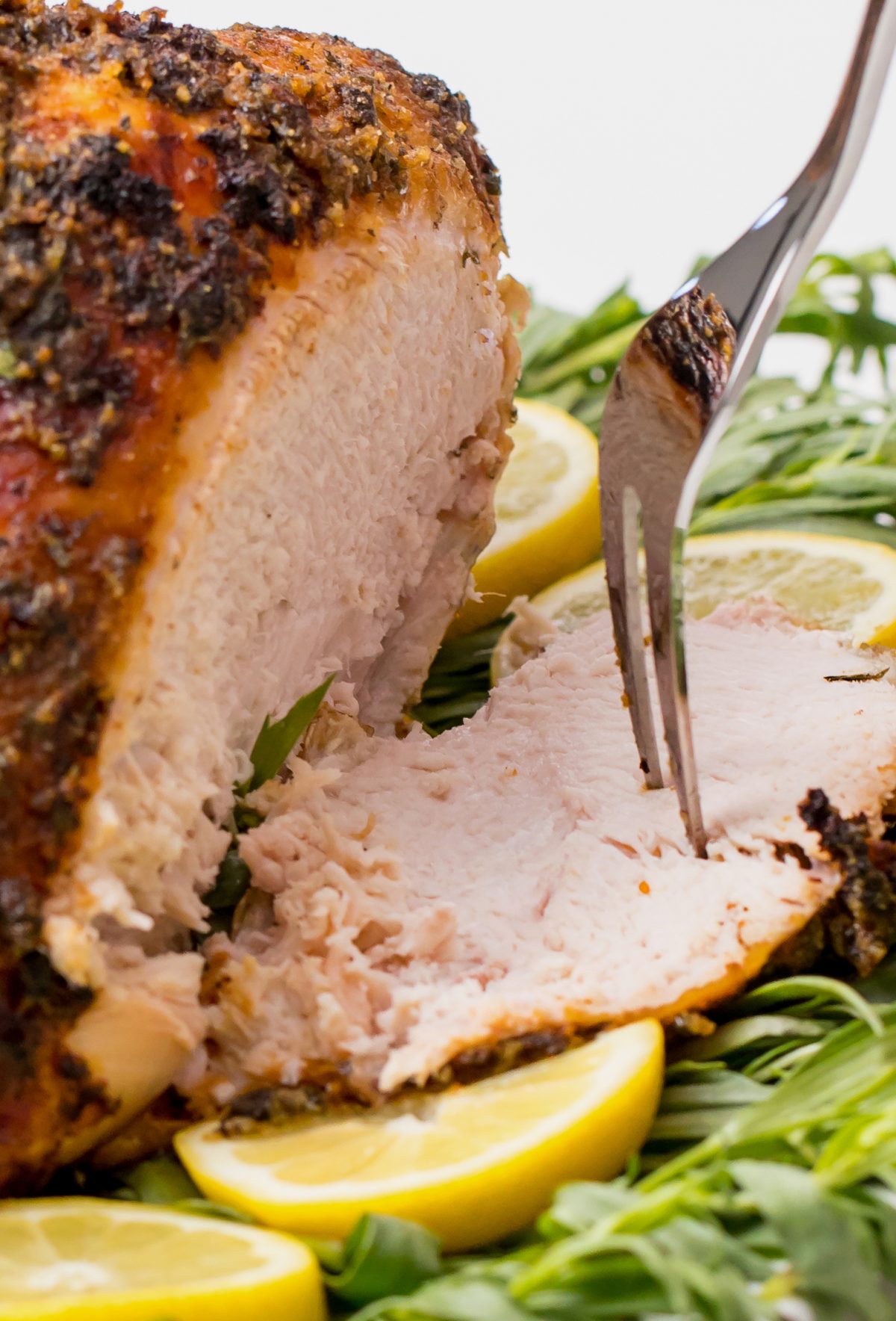 Tender and juicy grilled turkey breast - cutting a plated grilled turkey with sauce on on a bed of grass and lemons on a white table using a knife and fork