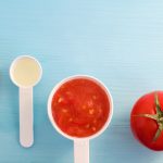 Plastic scoops with tomato puree and olive oil. Ingredients for preparing homemade facial mask. DIY cosmetics recipe. Top view, copy space.